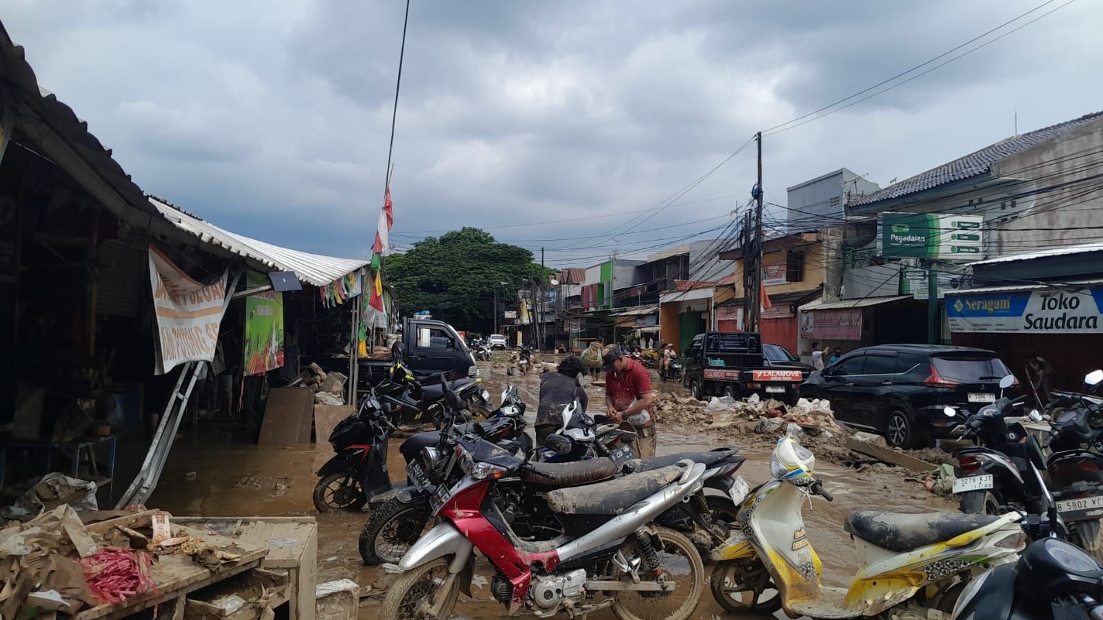 Doc. Kondisi banjir yang menggenangi ruas Jalan Pasar Bojong Kulur, Gunung Putri, Kabupaten Bogor, tampak menghambat aktivitas warga. Beberapa kendaraan sepeda motor terlihat terparkir di tengah genangan air, sementara pengendara dan pejalan kaki berusaha melewati jalan yang tergenang. (Bogor, 4/3/2025 – Foto Dokumentasi: M. Ismail).