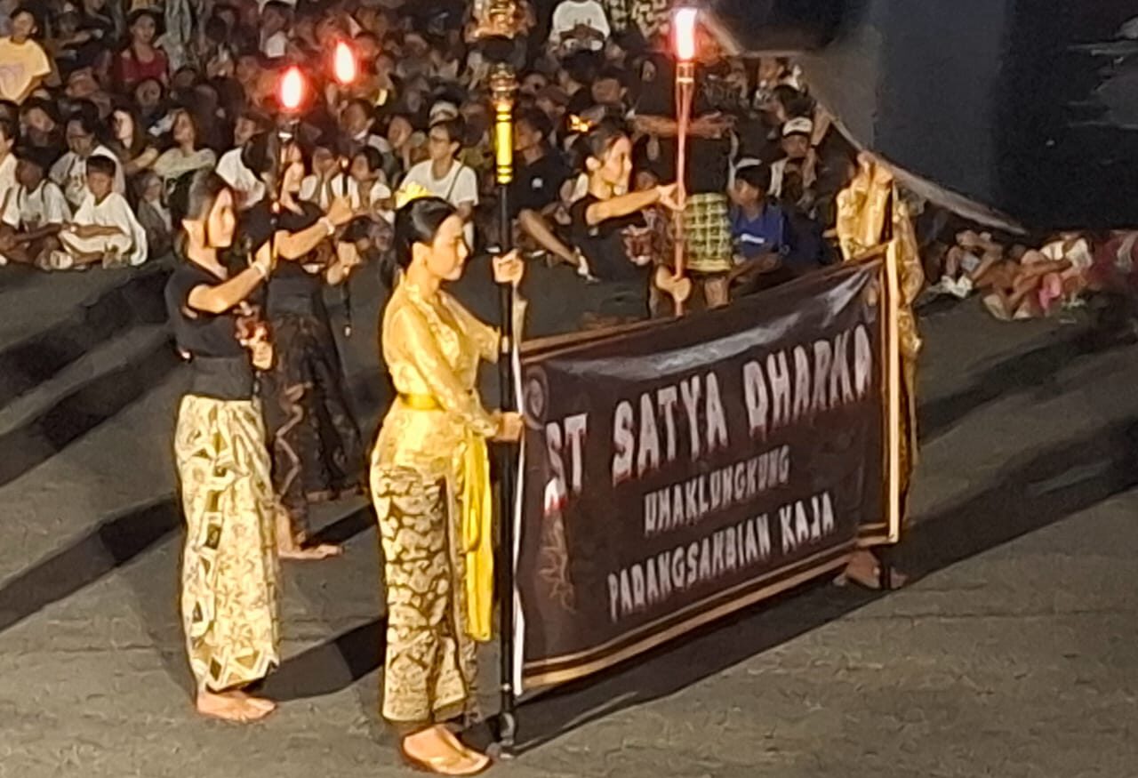 Doc. Sejumlah peserta mengenakan pakaian adat Bali membawa obor dan spanduk bertuliskan "ST SATYA DHARMA" dalam parade ogoh-ogoh di Padang Sambian. Mereka berjalan anggun di tengah sorotan cahaya, menambah sakralnya suasana acara. (Bali, 28/3/2025 - Foto Dokumentasi: Witanto).