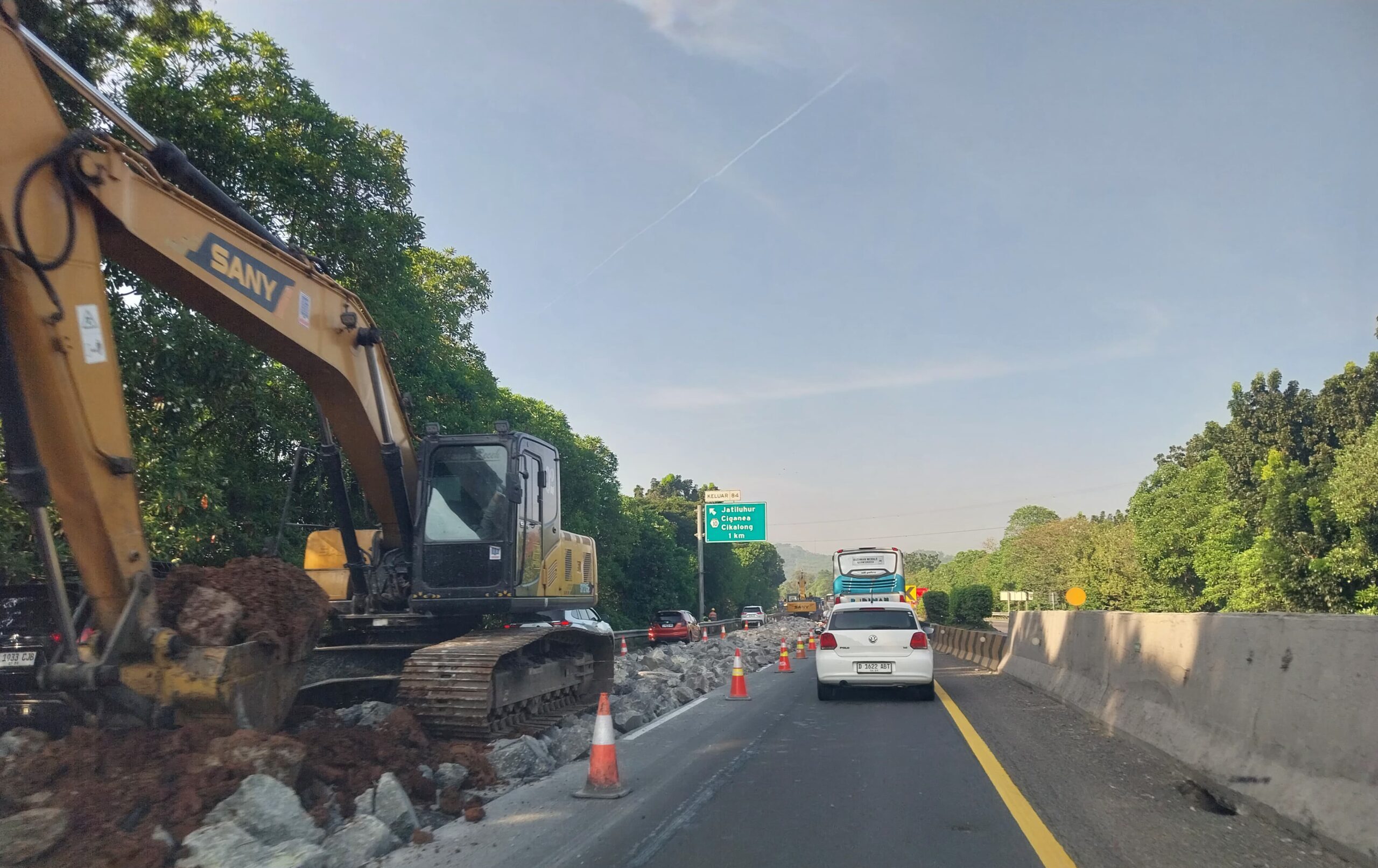 Doc. Sebuah ekskavator besar sedang memindahkan tanah dan batu di area perbaikan jalan. Lokasi masih berada di dekat papan petunjuk keluar KM 84, menunjukkan aktivitas intensif proyek perbaikan jalan. (Foto Dokumentasi: Nanda).
