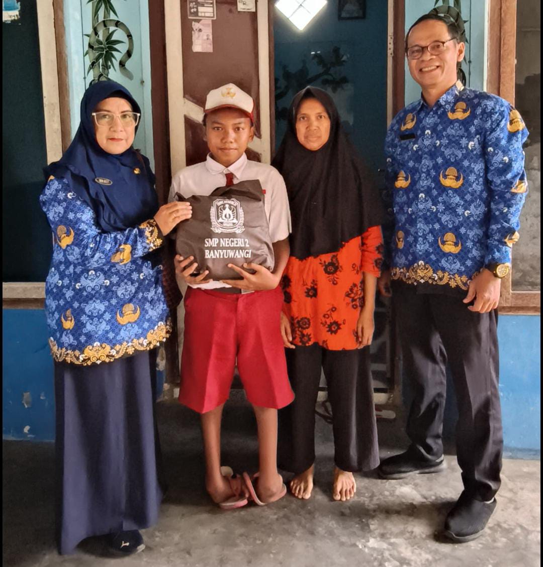 Doc. Kepala SMP Negeri 2 Banyuwangi, Dewi Astuti (kiri), menyerahkan seragam gratis kepada calon siswa jalur afirmasi di Kelurahan Sobo, Kecamatan Banyuwangi, didampingi wali murid dan guru sekolah, Selasa (20/5/2025). (Foto Dokumentasi: Ari Bagus. P).