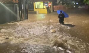Doc. Seorang warga melintasi genangan banjir setinggi paha saat hujan deras mengguyur wilayah Jabodetabek, Selasa dini hari (8/7/2025). Banjir terjadi akibat kombinasi curah hujan tinggi dan meluapnya aliran sungai di sejumlah titik. Meskipun perahu karet dari petugas sempat terlihat, sebagian besar warga memilih bertahan di rumah masing-masing. Banjir ini juga menyebabkan gangguan akses jalan, kerusakan fasilitas umum, dan menghambat aktivitas warga di beberapa kawasan terdampak. (Sumber Foto Dokumentasi: Kompas.com).