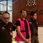 Doc. Seorang terduga tersangka kasus dugaan tindak pidana korupsi terlihat mengenakan rompi tahanan saat dibawa petugas Kejaksaan Agung untuk menjalani pemeriksaan lanjutan di Jakarta. Proses pengawalan dilakukan ketat oleh petugas sesuai prosedur penyidikan yang berlaku, sementara yang bersangkutan menuju kendaraan tahanan untuk pemeriksaan lebih lanjut.