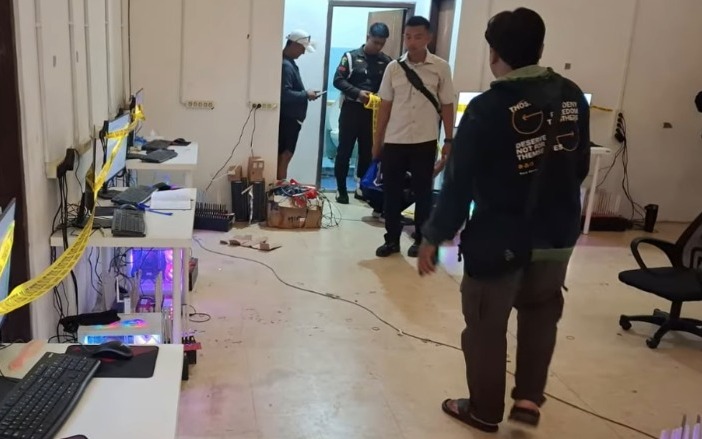 Lokasi rumah yang diduga digunakan sebagai markas judi daring di kawasan KPAD Cijantung, Jakarta Timur, dengan sejumlah komputer dan perangkat elektronik terlihat di atas meja dengan garis polisi. Foto ini menggambarkan kondisi lokasi yang dikaitkan dengan pengungkapan dugaan aktivitas judi online pada Minggu (4/10/2026)
